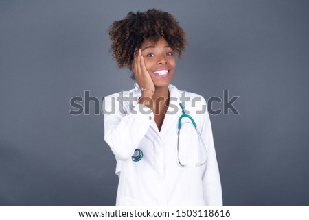 Amazement -  African American doctor woman excited looking to the side with hand on face. Surprised happy young woman looking sideways in excitement.
