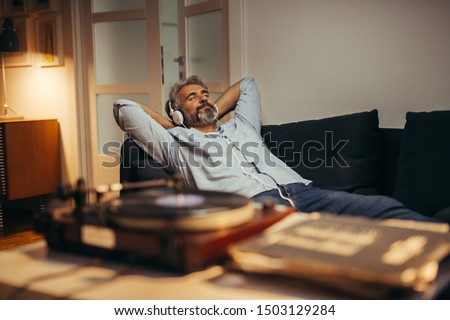 mid aged man listening music with headphones on record player, relaxed in sofa at his home Royalty-Free Stock Photo #1503129284