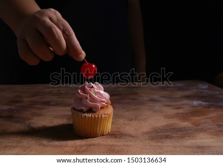    Putting a cherry on the pink cupcake on wooden table                             