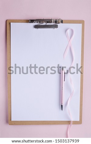 Clipboard, white blank paper, pink pen and pink ribbon as a symbol of breast cancer.Pink background, empty space for text