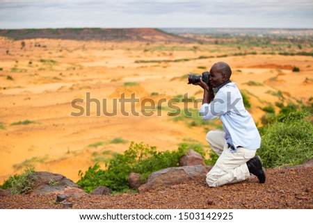 African man taking photos in the refreshed Sahel during summer rainy season under a cloudy sky outside Niamey capital of Niger