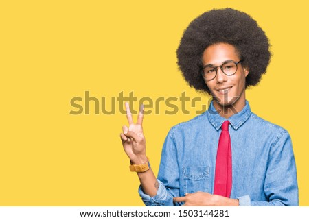 Young african american business man with afro hair wearing glasses and red tie smiling with happy face winking at the camera doing victory sign. Number two.