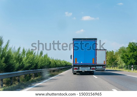 Cargo transportation concept.Highway view.Big truck driving fast on the asphalt road in sunny day in countryside landscape.Fast driving lorry  overtaking another truck.Clear blue sky view.
