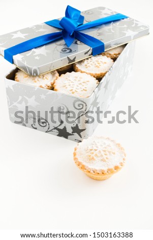 Closeup of mince pies in Christmas container with blue ribbon and bow isolated on white background.