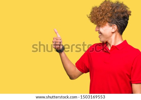 Young handsome man with afro hair wearing red t-shirt Looking proud, smiling doing thumbs up gesture to the side