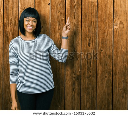 Beautiful young african american woman wearing stripes sweater over isolated background with a big smile on face, pointing with hand and finger to the side looking at the camera.