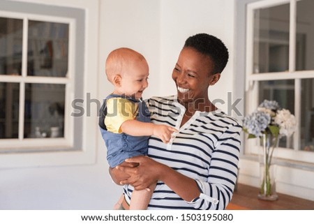 Portrait of happy black mother holding cute toddler laughing together at home. Cheerful african woman cuddling smiling little boy in hand and playing. Mature black nanny playing with little boy. Royalty-Free Stock Photo #1503195080