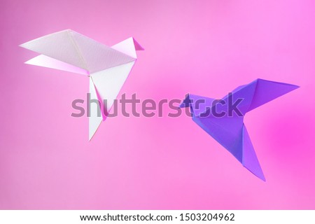 Origami paper two doves on a pastel pink background. Violet and white dove. The concept of arts and crafts, activities for children. Minimalism, levitation, place for text. Bright trend neon light.