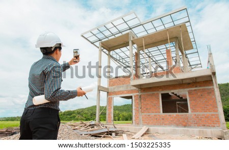 Asian manager of engineer architects in white helmet safety on construction site standing check a plan and project and take photo on smartphone