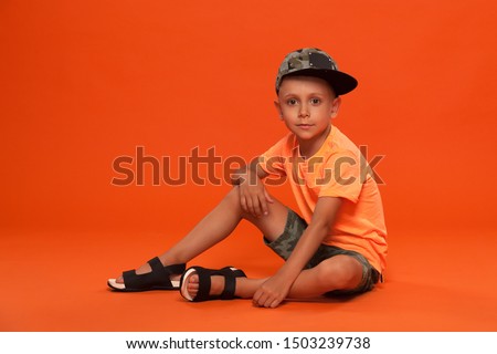 kid guy in cap and shorts on orange background