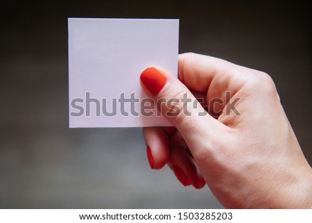 Female manicured hand is holding white empty square card. Soft focus. 