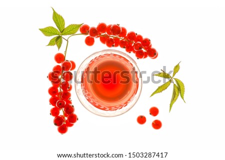 Overhead shot of a  backlit glass of red currant juice with fresh berries and leaves on a translucent lightbox.