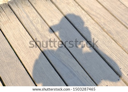 Shadow of a female photographer wearing a hat with a reflection on a wooden floor.