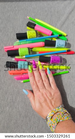 Female hand with long nails and multi-colored bright neon bottle manicure with nail polish and pen markers