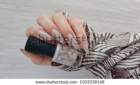 Female hand with long nails and a bottle of beige pink nail polish