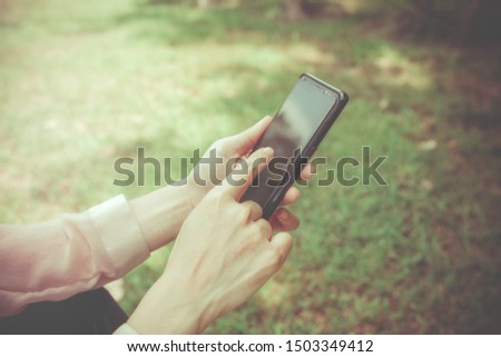 
Smartphone Concept Everywhere, Woman uses her hand to touch the screen to search for messages or other information in the application while sitting on the green lawn.

