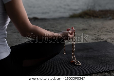 Beautiful young woman is practicing meditation on the river with her mala Royalty-Free Stock Photo #1503390347