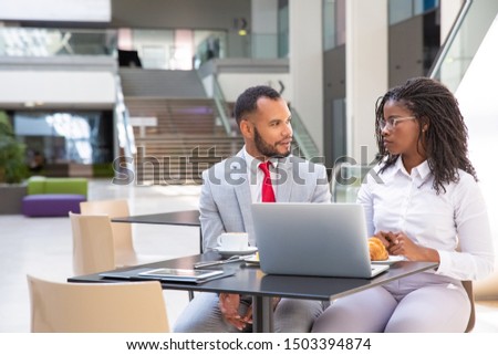 Diverse office employees discussing project during breakfast. Business man and woman sitting at laptop in cafe and talking. Communication concept