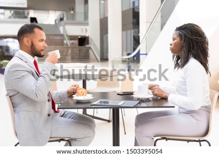 Diverse partners or colleagues meeting over cup of coffee. Side of business man and woman sitting at table in cafe, drinking coffee and talking. Business meeting or coffee hour concept