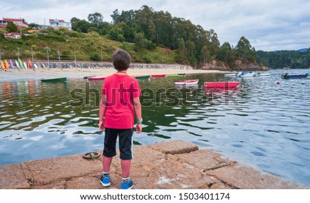Boy with red jacket in a port of a fishing village in Galicia. Ares Spain