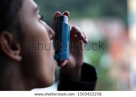 Health and medicine - Young girl using blue asthma inhaler to prevent an asthma attack. Pharmaceutical product to prevent and treat asthma. Royalty-Free Stock Photo #1503422258