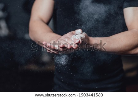 Beautiful handsome young athlete dressed in black t-shirt. During this time, sitting on the tires and applying talcum to your hands in the gym.