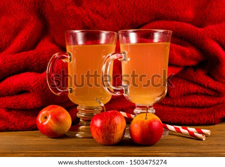 Hot apple cider in the glass mugs with striped straws and apple fruits on a red background.