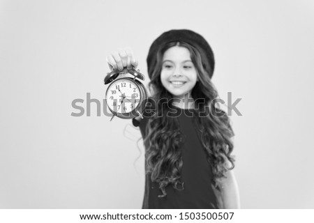 parisian child on yellow. beauty hairdresser. child with alarm clock. Timeless fashion. happy girl with long curly hair in beret. little girl in french style hat. time management. time to design.