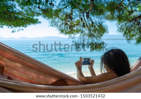 Young girl taking a picture with a smartphone lying in a hammock