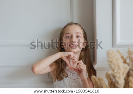 Beautiful little girl shows with gestures 'I love you'.A girl shows love.Cute girl in a white dress shows a heart with hands.Portrait of a little girl in the Studio with a white background.