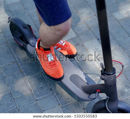 Man's legs are staying on the electric scooter in the park