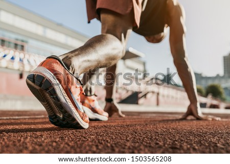 Close up of male athlete getting ready to start running on track . Focus on sneakers