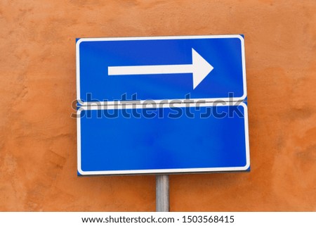 One way directional white arrow sign with an empty additional panel against a red wall.