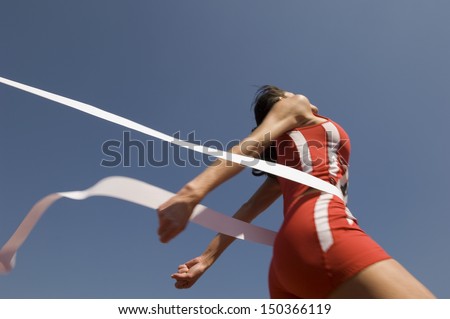 Low angle view of young female athlete crossing finish line against clear blue sky Royalty-Free Stock Photo #150366119