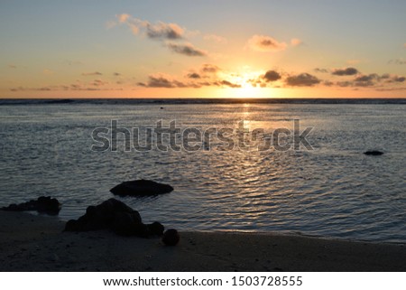 Stunning but simple sunset on a tropical island with rocks on the white sand beaches overlooking a coral reef in the Pacific Ocean on Rarotonga in the Cook Islands.