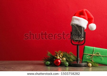 Microphone with Santa hat and decorations on grey table against red background, space for text. Christmas music Royalty-Free Stock Photo #1503758282