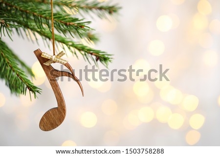 Fir tree branch with wooden note against blurred lights, space for text. Christmas music Royalty-Free Stock Photo #1503758288
