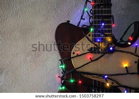 Guitar with colorful lights on grey stone background, space for text. Christmas music