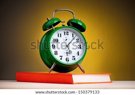 Big green alarm clock with red book on dark yellow background