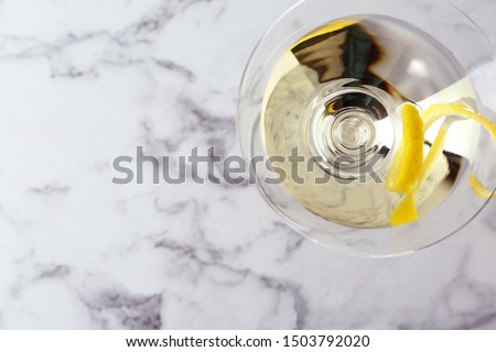 Glass of lemon drop martini cocktail with zest on white marble table, top view. Space for text