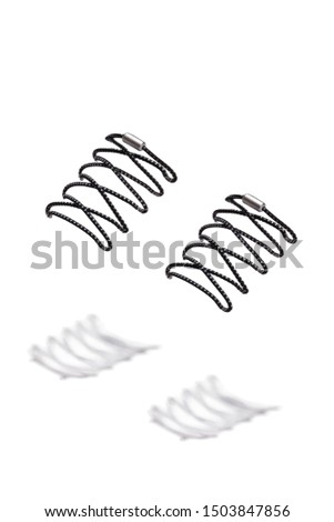 The photo of black spotted shoelaces with silver tips, hanging in the air on a white background. Shoelaces is casting a shadow. 