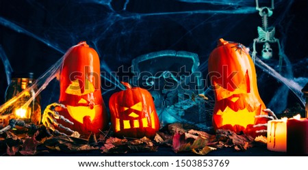 Halloween decor, Jack's Lantern band with glowing eyes, mystical glow, spider web,dry leaves, dark background, burning candles, skeleton bones