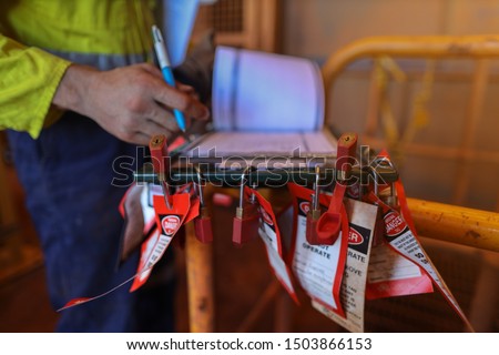 Personnel red locks attached with danger tag together with safety isolation permit lock box and defocused supervisor permit holder checking co- worker names to ensure their have sign on sheet  Royalty-Free Stock Photo #1503866153
