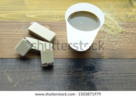 Picture of hot coffee in a paper cup with sugar and wafers on the table.