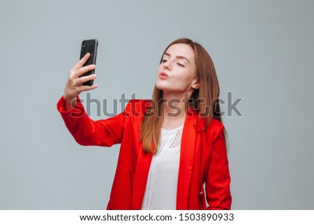 girl in a red jacket takes a selfie on the phone on a gray background
