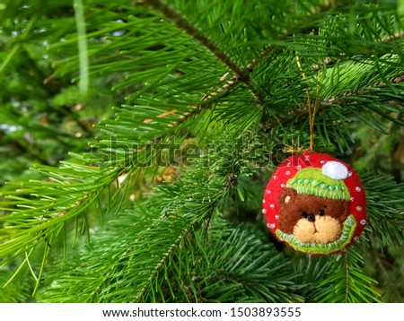 Handmade bauble figurines of bear. Christmas felt decoration on a spruce branch. Holiday background with a copy space.