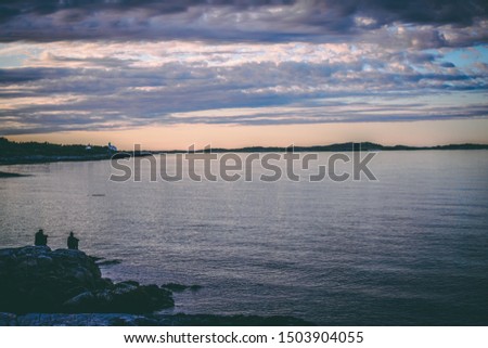 Photo of people sitting on a rocky seashore at sunset in Norway