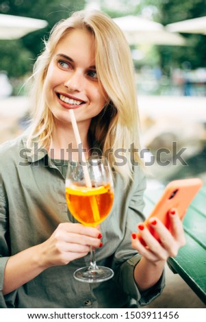 Photo of cheerful blonde with cocktail and phone in her hands on street