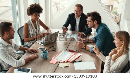 Sharing new ideas. Group of young business people discussing something and smiling while sitting at the office table Royalty-Free Stock Photo #1503919103