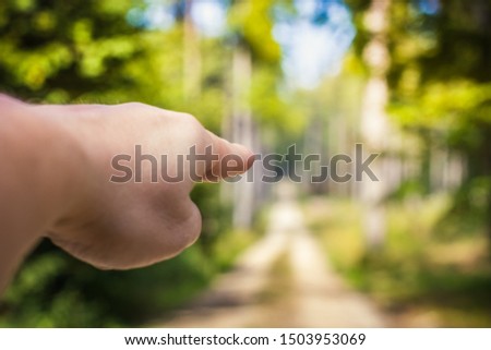 Left hand of a white man points forward. Caucasian person pointing in the direction of the horizon. Sunny day in the forest.